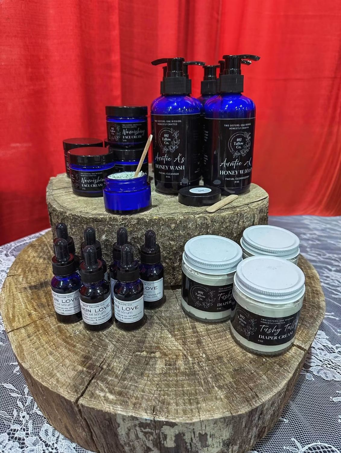 The 402 Tallow Co. product range displayed on wooden rounds: face creams, honey wash pump bottles, facial serum droppers and diaper cream jars, each with a black label carrying the script logo.